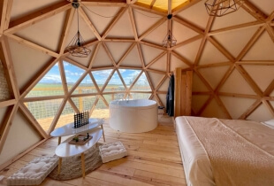 Vue de l'intérieur d'une chambre d'un dôme géodésique de 5m avec une partie de la toile transparente qui permet de voir le paysage