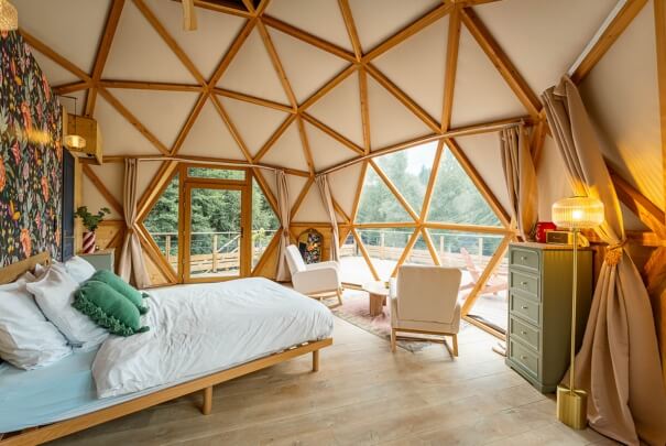 Un coin nuit confortable aménagé dans l'un des dômes géodésiques en Suisse, avec vue sur le paysage grâce à une toile transparente
