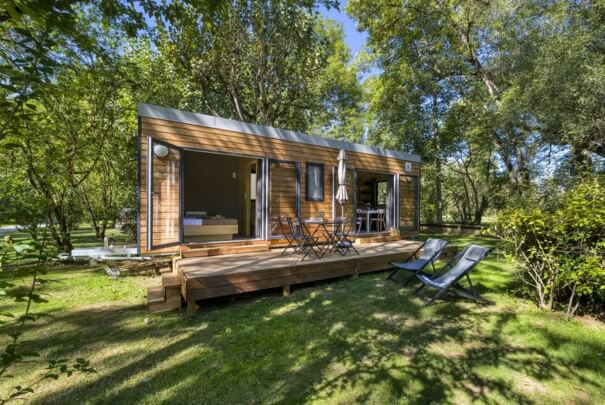 Tiny house l'indépendante installée au milieu des arbre avec sa terrasse et des chaises longues installées dans l'herbe
